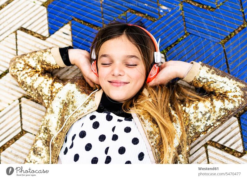 Portrait of happy girl wearing golden sequin jacket listening music with headphones coat coats jackets portrait portraits sequins females girls Gold Color