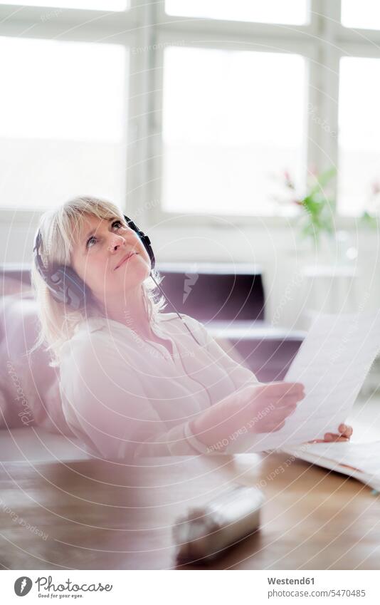 Relaxed mature businesswoman wearing headphones at desk looking up businesswomen business woman business women relaxed relaxation desks headset view seeing