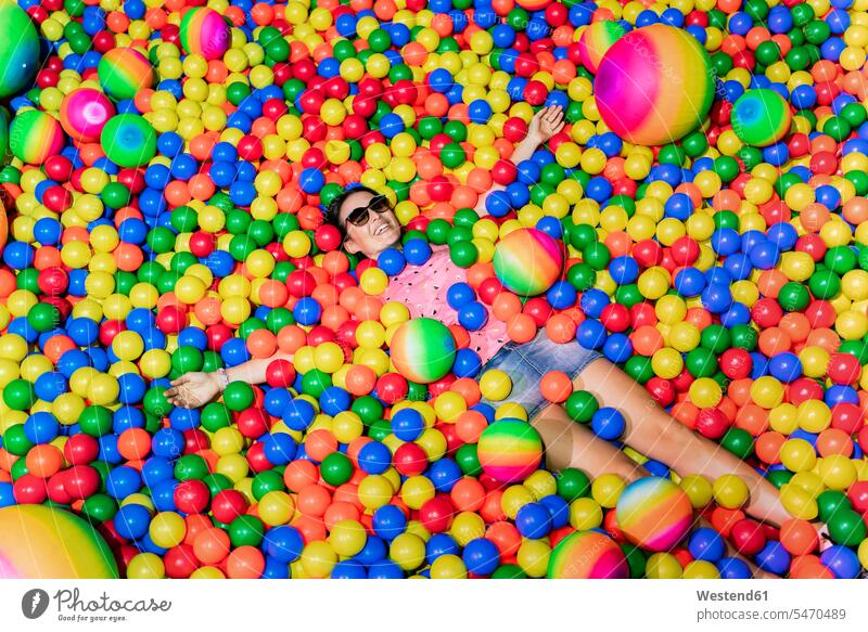 Portrait of happy woman lying among many colourful balls plastic toys Eye Glasses Eyeglasses specs spectacles Pair Of Sunglasses sun glasses play hide delight