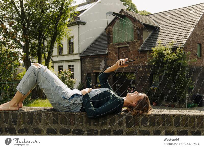 Young woman lying on a brick wall at a farmhouse using smartphone telecommunication phones telephone telephones cell phone cell phones Cellphone mobile