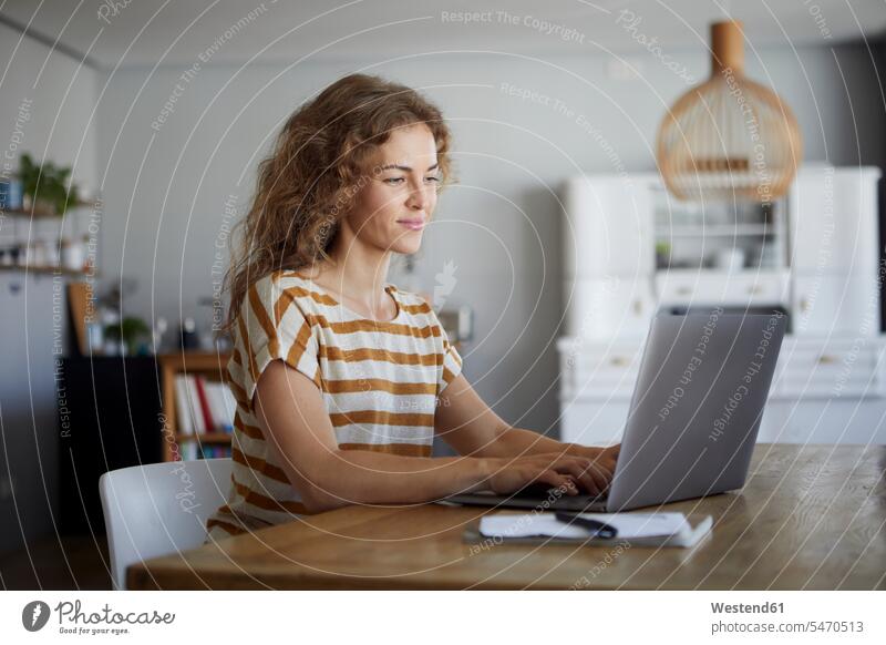Mid adult woman working on laptop while sitting by table at home color image colour image indoors indoor shot indoor shots interior interior view Interiors day