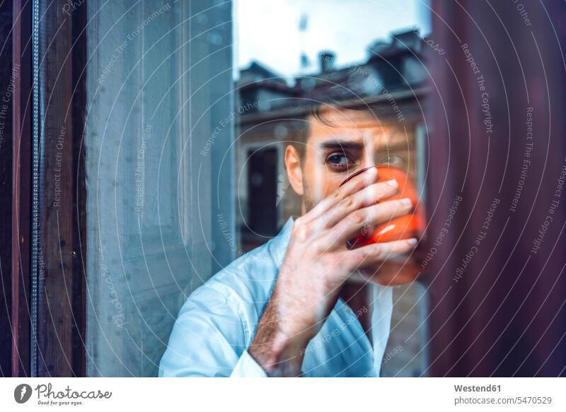 Young man holding cup looking out of window human human being human beings humans person persons celibate celibates singles solitary people solitary person
