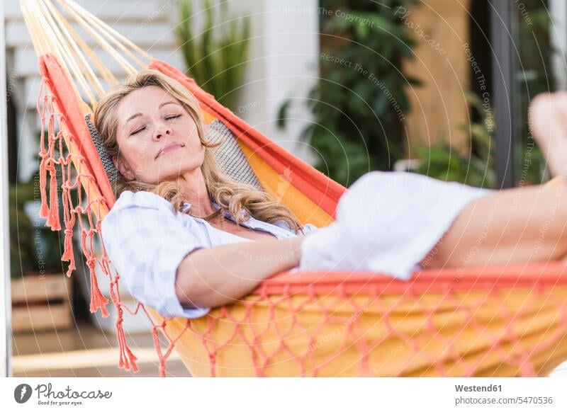 Portrait of mature woman with eyes closed relaxing in hammock on terrace hammocks enjoy enjoyment indulgence indulging savoring laying down lie lying down