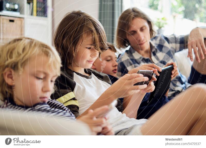 Father looking at boys playing games on smart phones and digital tablet in living room color image colour image indoors indoor shot indoor shots interior