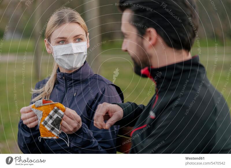 Young woman giving face mask to man while sitting at park during quarantine color image colour image outdoors location shots outdoor shot outdoor shots day