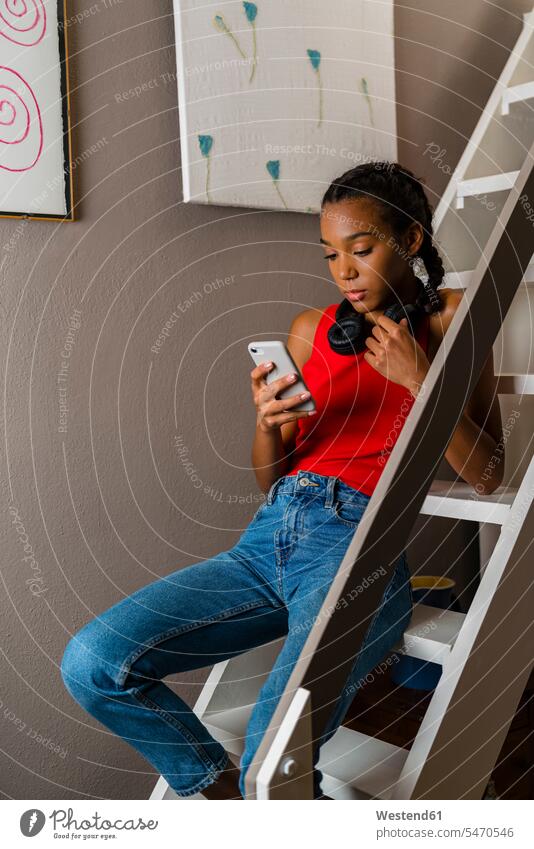 Teenage girl using smart phone while sitting on ladder at home color image colour image indoors indoor shot indoor shots interior interior view Interiors day