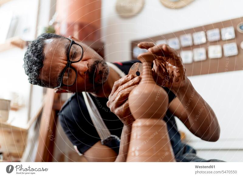 Close-up of male artist making earthenware while sitting in workshop color image colour image Spain indoors indoor shot indoor shots interior interior view