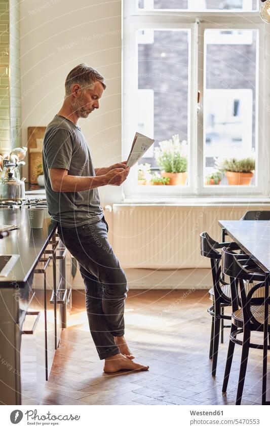 Mature man reading newspaper in kitchen at home human human being human beings humans person persons celibate celibates singles solitary people solitary person