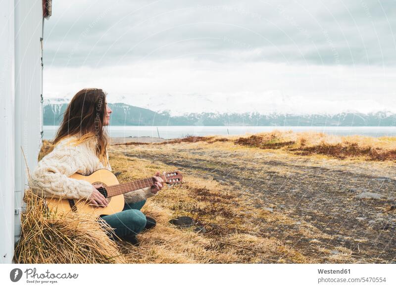 Iceland, woman sitting in rural landscape playing guitar guitars landscapes scenery terrain females women Seated country countryside stringed instrument