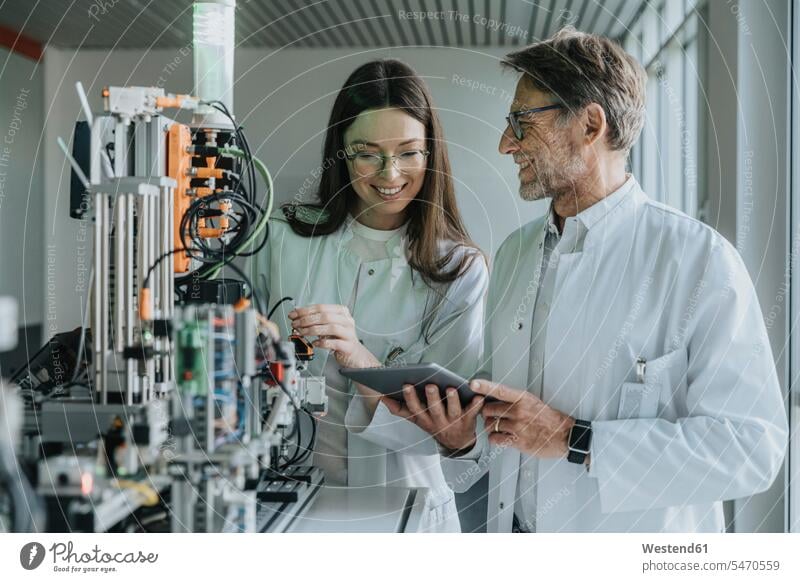 Mature man showing digital tablet to female colleague while standing by machinery in laboratory color image colour image indoors indoor shot indoor shots