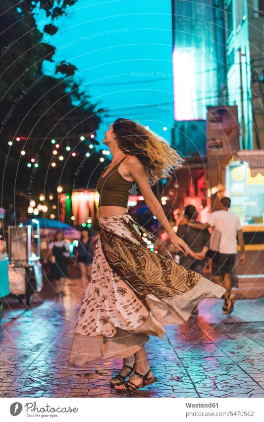 Thailand, Bangkok, young woman in the city dancing on the street at night by night nite night photography town cities towns dance road streets roads females