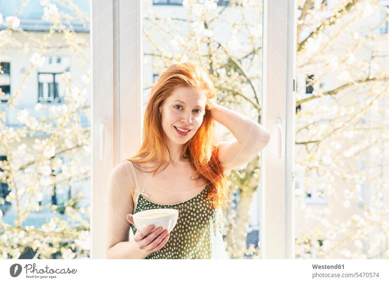 Portrait of redheaded woman with bowl of white coffee in front of window portrait portraits windows red hair red hairs red-haired females women Coffee