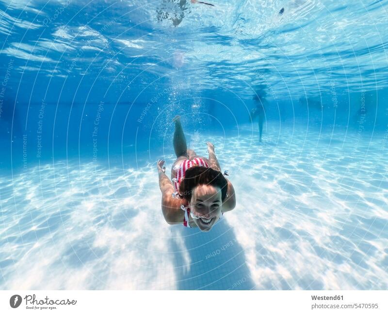 Happy woman swimming underwater in pool at tourist resort color image colour image day daylight shot daylight shots day shots daytime leisure activity