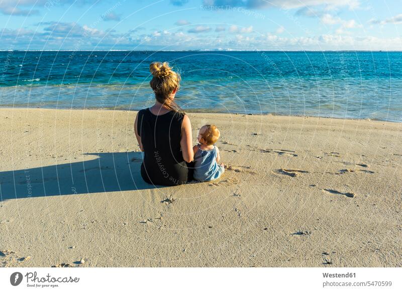 Cook islands, Rarotonga, Woman sitting with her baby on a white sand beach Seated daughter daughters together Travel beaches mother mommy mothers mummy mama