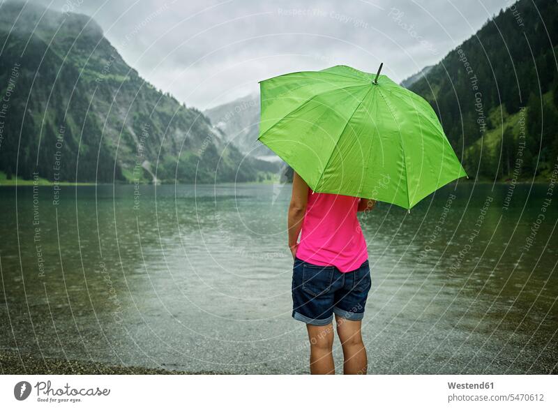 Mature woman standing with green umbrella at Vilsalpsee lakeshore during rainy season color image colour image Austria outdoors location shots outdoor shot