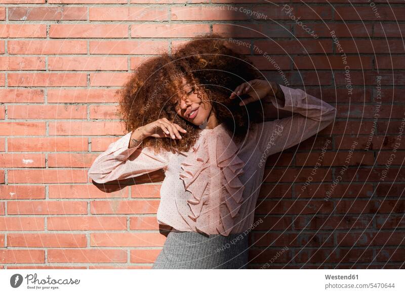 Portrait of beautiful young woman with afro hairdo at brick wall in sunshine Afro sunlight Sunlit portrait portraits females women hairstyle hair-dos hairstyles