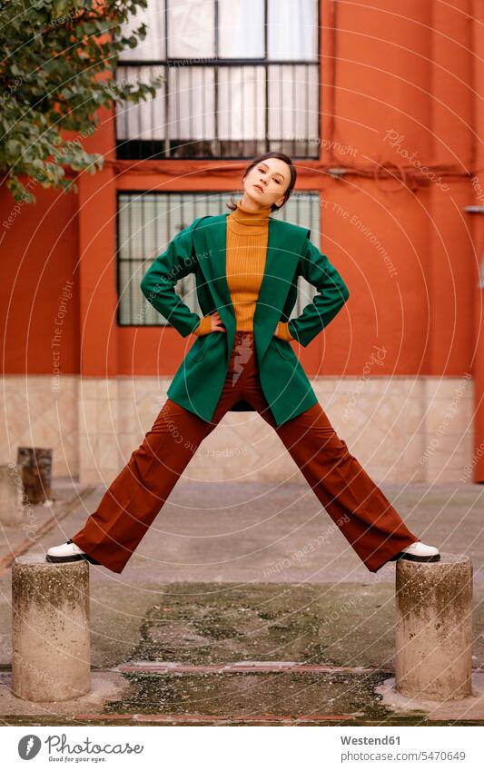 Young woman wearing green jacket standing on bollards against building in city color image colour image Spain casual clothing casual wear leisure wear