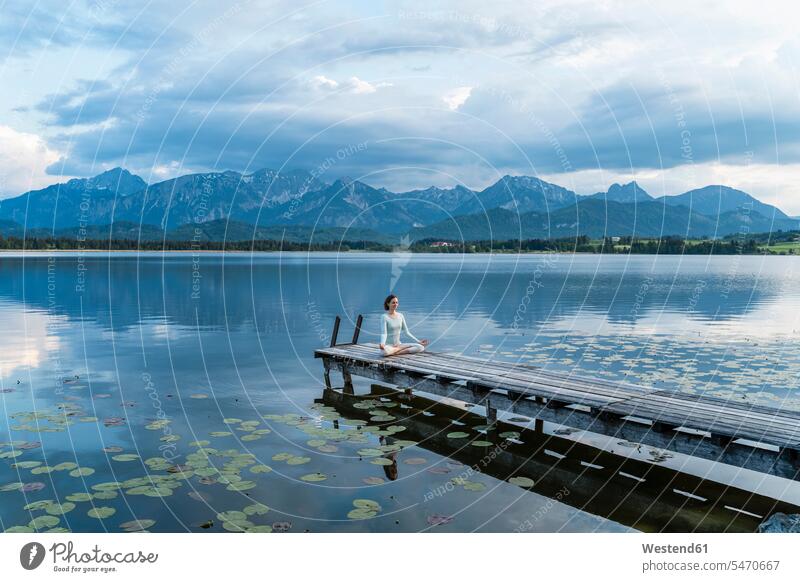 Woman meditating while sitting on jetty over lake against mountains color image colour image Germany leisure activity leisure activities free time leisure time