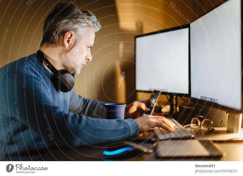 Mature man sitting at desk at home working with smartphone and computer Occupation Work job jobs profession professional occupation jumper sweater Sweaters