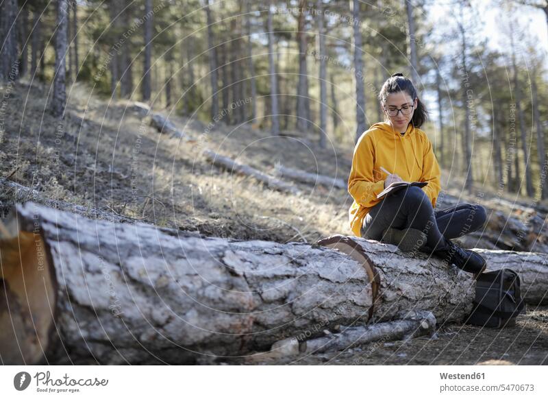 Young woman with yellow sweater in the forest, writing diary diaries females women notebook notebooks female hiker female wanderers write sitting Seated Adults