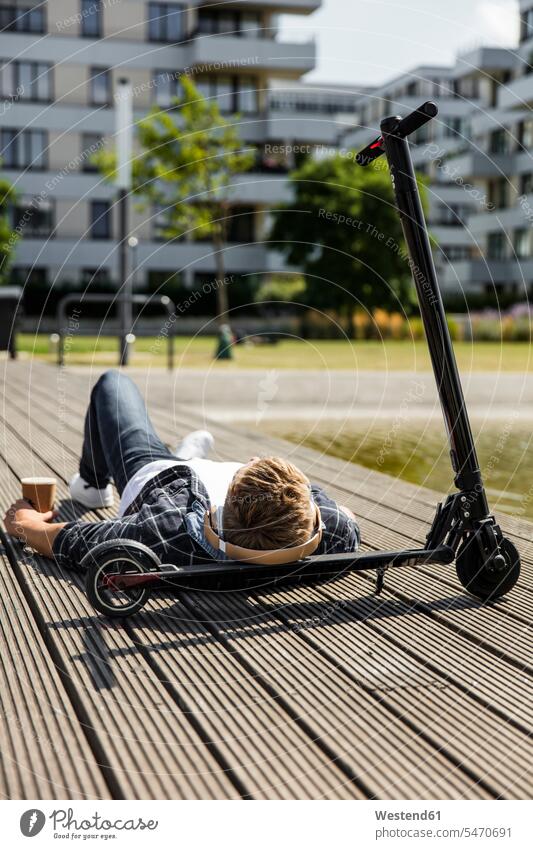 Young man with e-scooter lying on boardwalk business life business world business person businesspeople Business man Business men Businessmen headphone headset