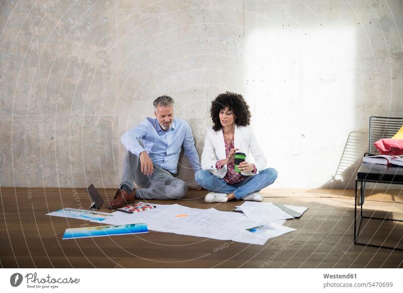Businessman and businesswoman sitting on the floor in a loft discussing documents talking speaking Business man Businessmen Business men discussion Seated