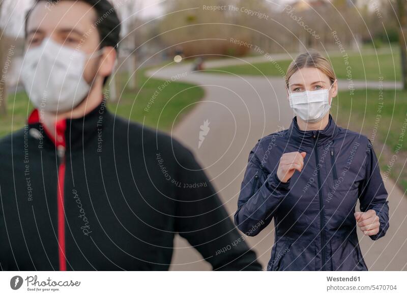 Young man and woman wearing face mask while jogging on footpath at park during COVID-19 color image colour image outdoors location shots outdoor shot