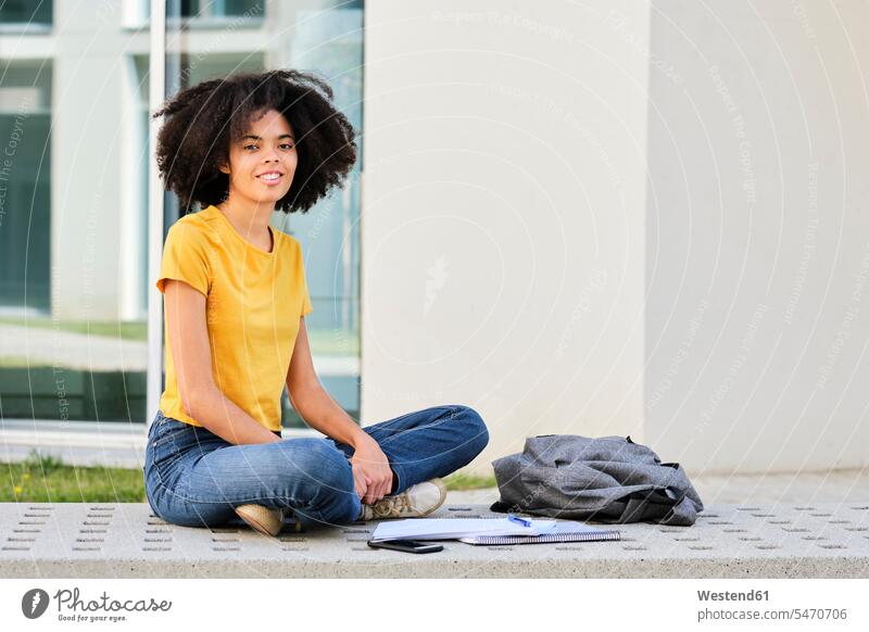Young university student sitting with cross-legged by books and bag at campus color image colour image outdoors location shots outdoor shot outdoor shots day