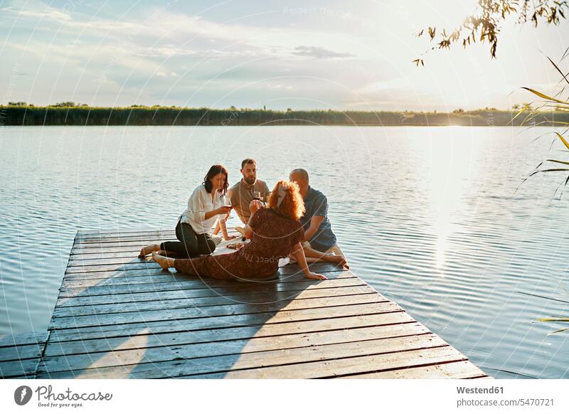 Friends having picnic on jetty at a lake at sunset human human being human beings humans person persons caucasian appearance caucasian ethnicity european Group