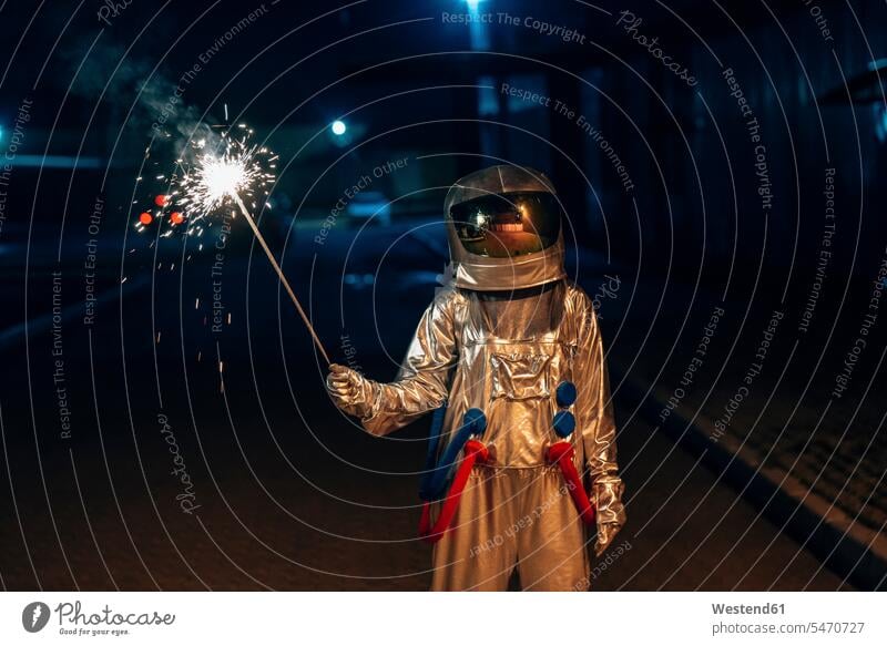 Spaceman standing outdoors at night holding sparkler sparklers by night nite night photography spaceman spacemen astronaut astronauts astronautics space travel