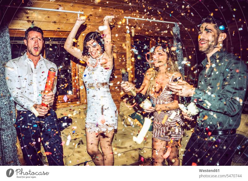 Happy friends opening champagne while dancing amidst confetti in party color image colour image indoors indoor shot indoor shots interior interior view