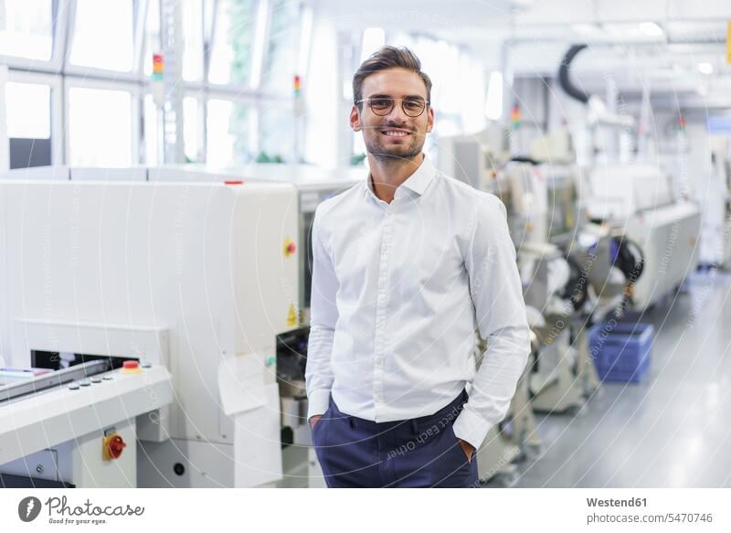 Smiling young businessman standing with hands in pockets at illuminated factory color image colour image indoors indoor shot indoor shots interior interior view