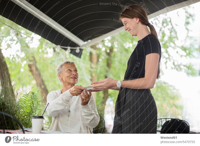 Waitress handing over plate to smiling senior woman at an outdoor cafe giving give present Handing handing out presenting hand over senior women elder women