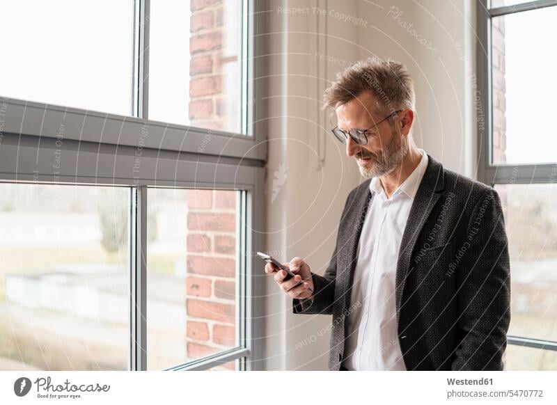 Businessman using cell phone at the window in office mobile phone mobiles mobile phones Cellphone cell phones Business man Businessmen Business men offices