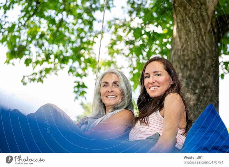 Portrait of two smiling women relaxing on a hanging bed in garden portrait portraits beds gardens domestic garden relaxed relaxation woman females