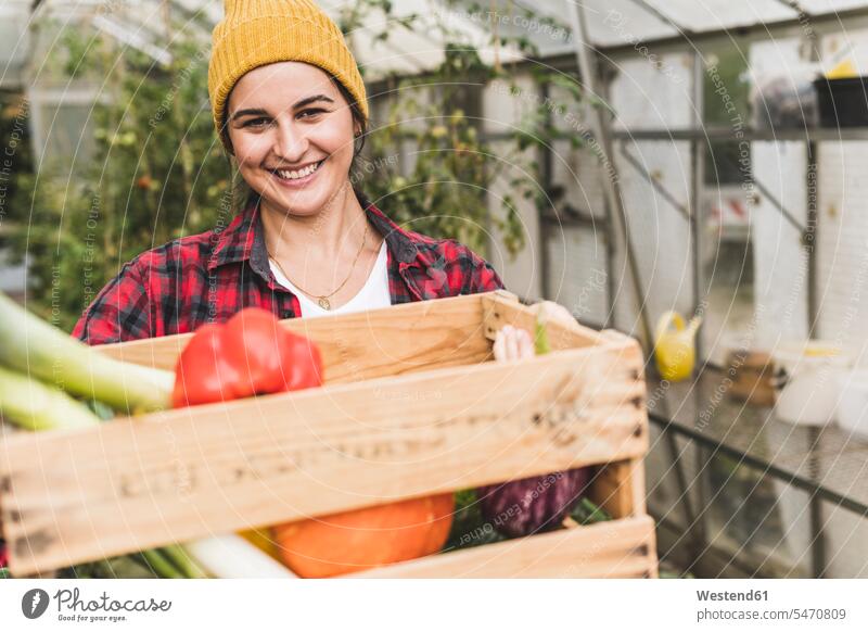 Smiling woman carrying crate with vegetables while standing against greenhouse color image colour image Germany casual clothing casual wear leisure wear