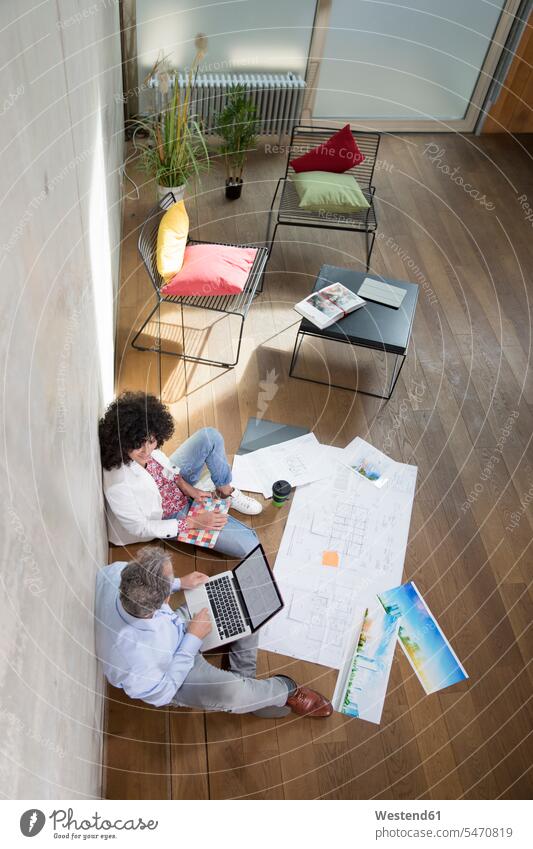 Businessman and businesswoman sitting on the floor in a loft working with laptop and documents Seated At Work floors Business man Businessmen Business men