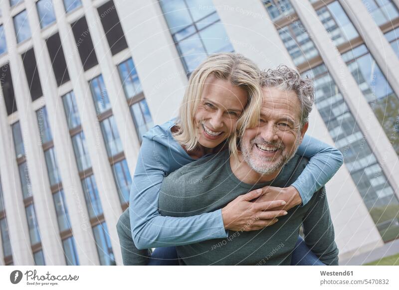 Happy mature man carrying woman piggyback in the city jumper sweater Sweaters embrace Embracement hug hugging Ardor Ardour enthusiasm enthusiastic excited relax