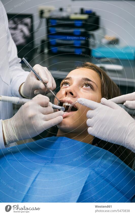 Dentist in surgical gloves doing dental treatment of female patient with help of assistant at clinic color image colour image indoors indoor shot indoor shots