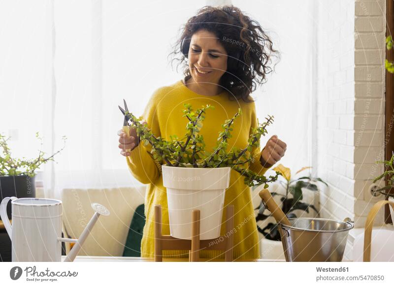 Woman at home wearing headphones and pruning plants human human being human beings humans person persons curl curled curls curly hair windows jumper sweater