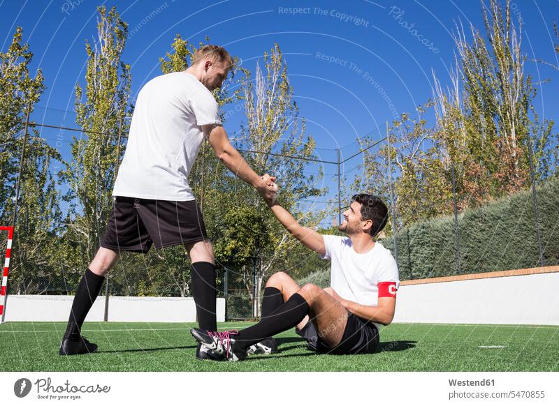 Football player helping an injured player during a match football ground soccer pitch football pitch assistance assisting Help football player footballers