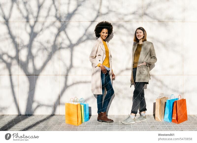 Portrait of two happy women with shopping bags standing at a wall walls woman females happiness portrait portraits shopping-bag shopping-bags female friends