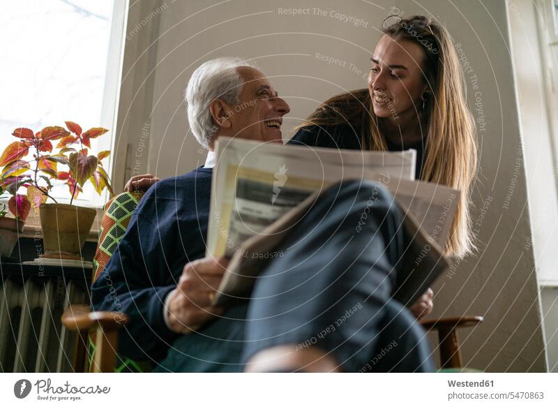 Happy young woman and senior man with newspaper at home generation windows newspapers chairs read smile Seated sit delight enjoyment Pleasant pleasure