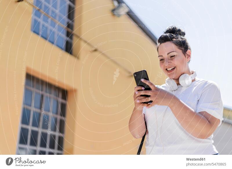 Happy curvy young woman with headphones using mobile phone in the city human human being human beings humans person persons caucasian appearance