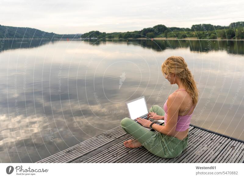 Young woman using laptop on a jetty at a lake Occupation Work job jobs profession professional occupation computers Laptop Computer Laptop Computers laptops
