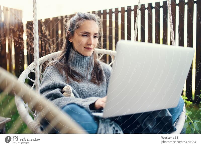 Beautiful young woman using laptop while sitting on swing in garden color image colour image leisure activity leisure activities free time leisure time outdoors