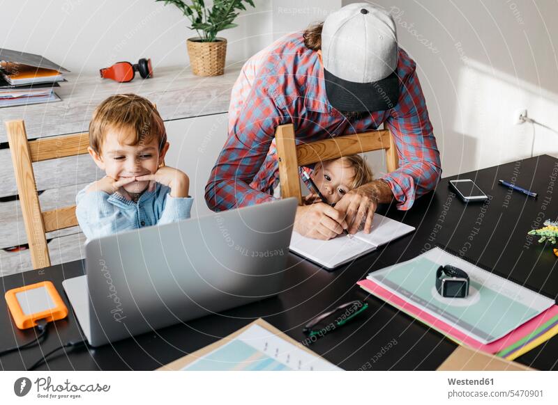Father writing in notebook while children are playing at his desk daughter daughters desks son sons manchild manchildren notebooks write father pa fathers daddy