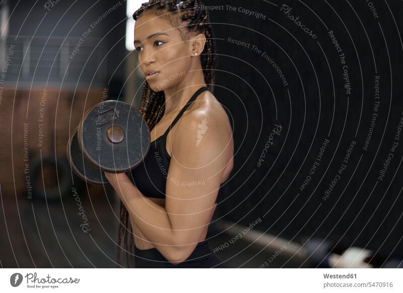 Confident female athlete lifting dumbbells looking away while standing in gym color image colour image South Africa indoors indoor shot indoor shots interior