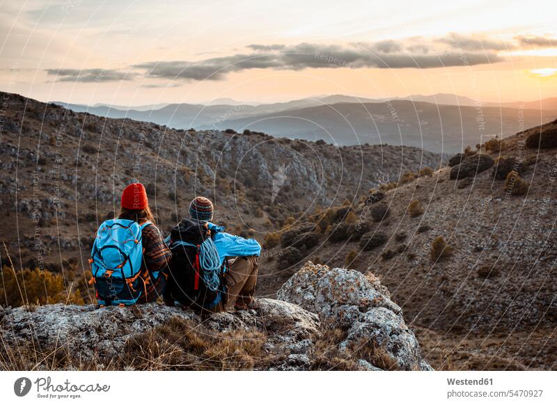 Male and female hikers enjoying sunset while sitting on rock mountain during vacation color image colour image outdoors location shots outdoor shot