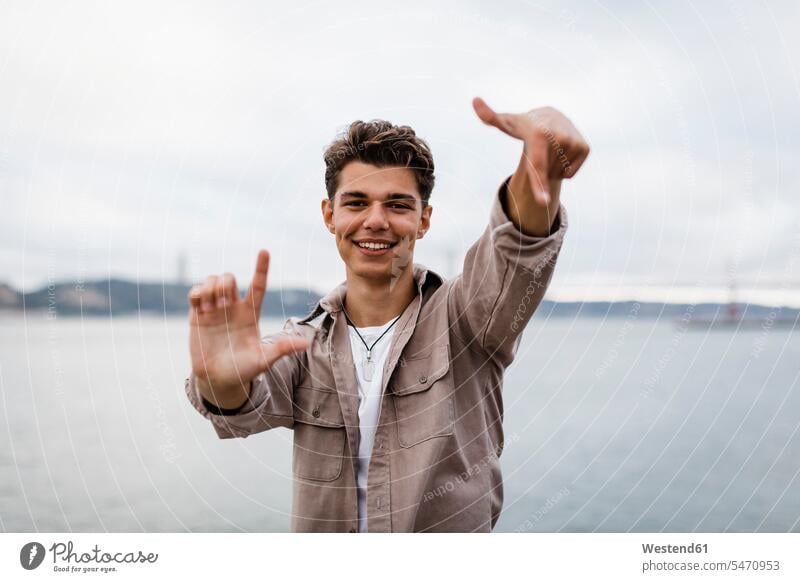 Smiling young man showing hand signs against sky color image colour image Portugal outdoors location shots outdoor shot outdoor shots day daylight shot